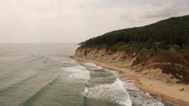 Karadeniz 'deki kumsal, kayalık dağlar üzerindeki hava aracı yoğun ormanı parlak güneşli bir günde görüyor. Bulgaristan 'ın 4k kıyısında dalgaların üzerinde alçaktan uçuyordu. yaz ılık hava sıcaklığı