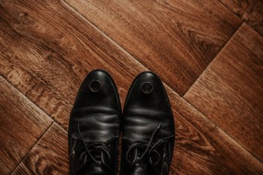 Erkekler klasik moda siyah ayakkabılar. Kahverengi desenli ahşap zeminde çizmeler. Damadın ayakkabılarında altın gümüş yüzükler var.