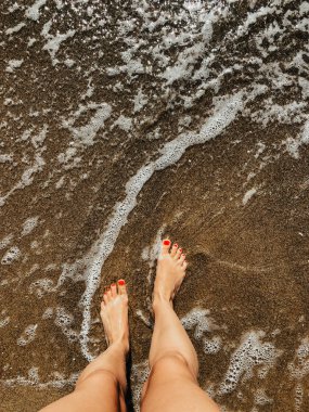 Yaz günü kumsalda, deniz köpüğü dalgalarında çıplak ayaklı bir kadın. Kadın ayağının üstündeki üst manzara. Okyanus berrak deniz köpüğü. Sahilde yaz tatili konsepti olan bir kız. Doğal duvar kağıdı