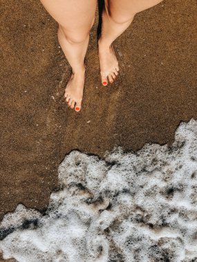 Yaz günü kumsalda, deniz köpüğü dalgalarında çıplak ayaklı bir kadın. Kadın ayağının üstündeki üst manzara. Okyanus berrak deniz köpüğü. Sahilde yaz tatili konsepti olan bir kız. Doğal duvar kağıdı