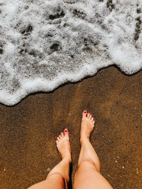 Yaz günü kumsalda, deniz köpüğü dalgalarında çıplak ayaklı bir kadın. Kadın ayağının üstündeki üst manzara. Okyanus berrak deniz köpüğü. Sahilde yaz tatili konsepti olan bir kız. Doğal duvar kağıdı