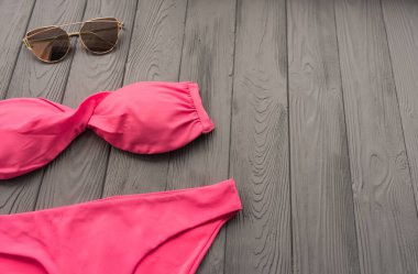 İki parçalı plaj mayosu giyen moda güneş gözlüğü takan bir kadın. Yaz arkaplan şablonu modelleme boş alan renkli kompozisyon örneği metni. Gri ahşap arkaplanın üstü.