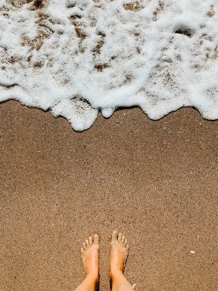 Yaz günü kumsalda, deniz köpüğü dalgalarında çıplak ayaklı bir kadın. Kadın ayağının üstündeki üst manzara. Okyanus berrak deniz köpüğü. Sahilde yaz tatili konsepti olan bir kız. Doğal duvar kağıdı