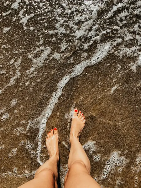 Yaz günü kumsalda, deniz köpüğü dalgalarında çıplak ayaklı bir kadın. Kadın ayağının üstündeki üst manzara. Okyanus berrak deniz köpüğü. Sahilde yaz tatili konsepti olan bir kız. Doğal duvar kağıdı