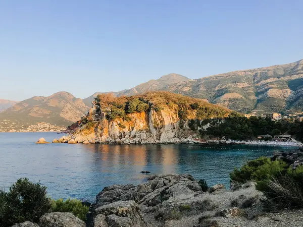 Karadağ Sutomore taşlarının tepesi güneş batarken Adriyatik deniz suyu dağlarının mavi turkuvaz plajını gösteriyor. Karadağ 'ın kayalık kıyı manzarası. Güzel gök mavisi okyanus. Yaz arkaplanı 