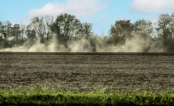 Farmer clearing out farmland with his large machinery leaving behind him a cloud of dust
