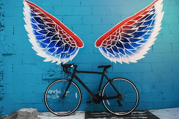 赤青と白の翼の落書きの壁に黒い道の自転車の貸出 — ストック写真