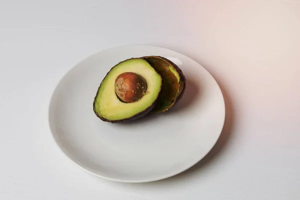 stock image Avocado cut in half on a white plate. A seed in an avocado.