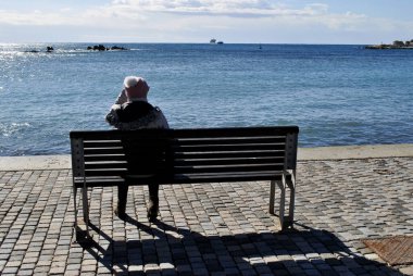 a woman in a hat sits on the bench on the beach.