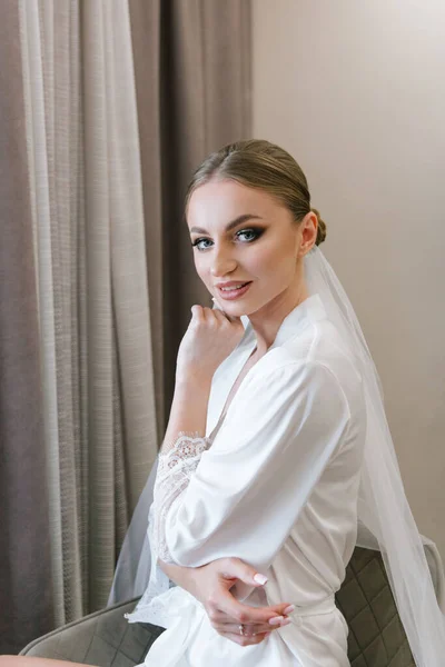 Fees for the wedding of a beautiful luxurious bride in a bathrobe with a wedding dress in a hotel, fashion portraits