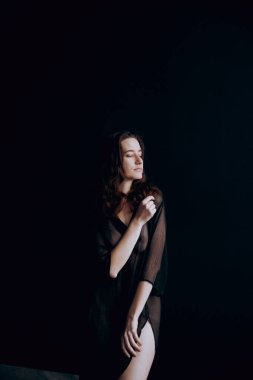 Beautiful, natural naked girl artistic posing at a stylish and fashionable nude photo shoot as a model in a photo studio with a transparent cape and bandage and looks like art