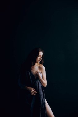 Beautiful, natural naked girl artistic posing at a stylish and fashionable nude photo shoot as a model in a photo studio with a transparent cape and bandage and looks like art