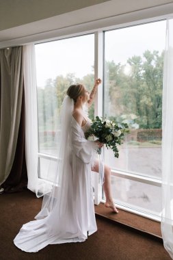 Güzelim, seksi bir gelinin iç çamaşırlı bir buketle sabah hazırlıkları. Bir otelde bornoz. Gelinlik giyip ayakkabılarını giydiği yer.