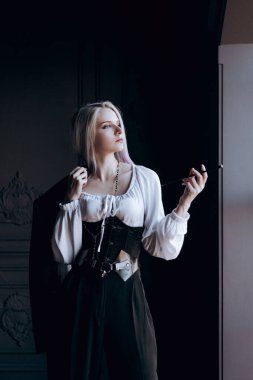 Luxurious girl with beautiful hair and tattoos in a hat and with a mouthpiece in a photo studio in a trouser suit.