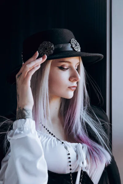Luxurious girl with beautiful hair and tattoos in a hat and with a mouthpiece in a photo studio in a trouser suit.