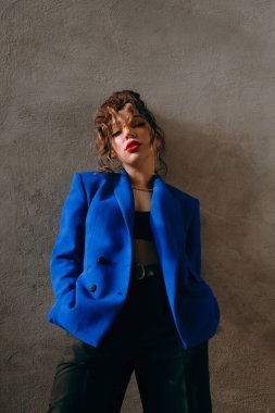 Güneş gözlüklü, ince vücutlu, mavi ceketli, yeşil elbiseli, şık, şık bir moda çekiminde fotoğraf stüdyosunda poz veren çekici bir kız..