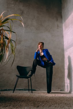 Güneş gözlüklü, ince vücutlu, mavi ceketli, yeşil elbiseli, şık, şık bir moda çekiminde fotoğraf stüdyosunda poz veren çekici bir kız..