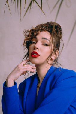 Güneş gözlüklü, ince vücutlu, mavi ceketli, yeşil elbiseli, şık, şık bir moda çekiminde fotoğraf stüdyosunda poz veren çekici bir kız..