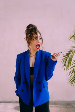 Güneş gözlüklü, ince vücutlu, mavi ceketli, yeşil elbiseli, şık, şık bir moda çekiminde fotoğraf stüdyosunda poz veren çekici bir kız..