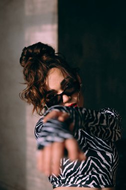 Güneş gözlüklü, ince vücutlu, mavi ceketli, yeşil elbiseli, şık, şık bir moda çekiminde fotoğraf stüdyosunda poz veren çekici bir kız..