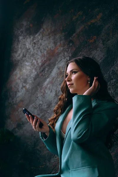 Luxurious girl with beautiful makeup and hairstyle, permanent makeup specialist, holds tools in her hands. Photoshoot in a photo studio in a suit, jeans and a shirt.