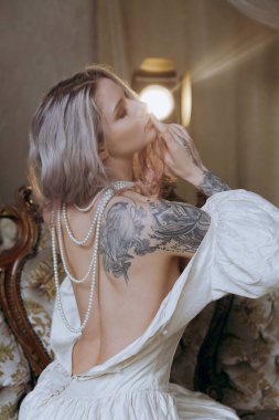 Kaliteli bir elbise içinde güzel bir makyajı ve saç stili olan lüks bir kız bir sabah yatağında uyanıp piyanonun yanındaki kanepede modellik yapıyor.