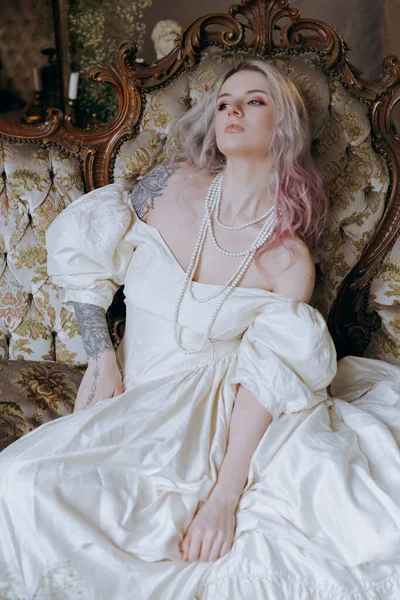 一个穿着老式衣服 化着漂亮妆容和发型的奢华女孩在床上醒来 坐在钢琴旁边的沙发上 摆出一副模特的模样 — 图库照片