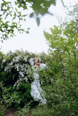Beyaz elbiseli, güzel, şık, tatlı sarışın. Yeşil desenli, kır gelini Spirea 'daki fotoğraf çekimi için model. Onlar parkın yeşil bahçesinde onun lüks portrelerini yaptılar..