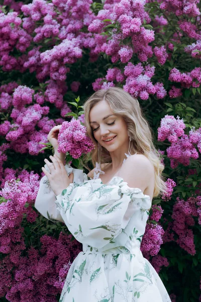 stock image Beautiful, stylish, cute blonde in a white dress with a green pattern as a model for a photo shoot in lilac. They made luxurious portraits of her in the green garden of the park.