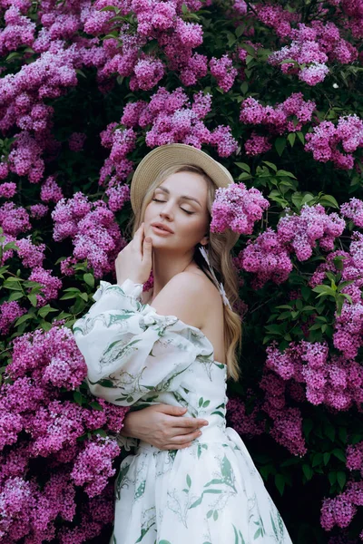 stock image Beautiful, stylish, cute blonde in a white dress with a green pattern as a model for a photo shoot in lilac. They made luxurious portraits of her in the green garden of the park.