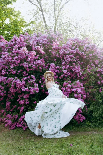可爱的金发美女穿着绿色图案的白色连衣裙 是紫丁香拍照的模特 他们在公园的绿色花园里为她画了许多豪华的肖像 — 图库照片