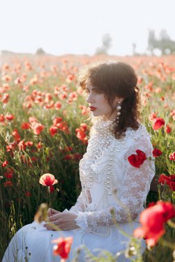 Modellik yapan beyaz elbiseli güzel bir kız, gün batımında gelincik tarlasında moda fotoğraf çekiminde..