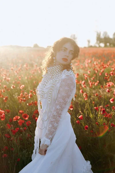 一个穿着老式白色连衣裙的漂亮女孩 作为模特 在夕阳西下的罂粟地里拍摄时尚照片 — 图库照片
