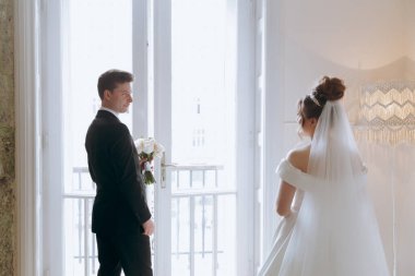 Damadın siyah takım elbiseli ilk buluşması ve beyaz gelinlikli gelinin beyaz ve siyah arka planda bir fotoğraf stüdyosunun içinde bir buket olması.