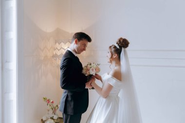 Damadın siyah takım elbiseli ilk buluşması ve beyaz gelinlikli gelinin beyaz ve siyah arka planda bir fotoğraf stüdyosunun içinde bir buket olması.