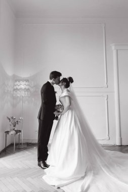 Damadın siyah takım elbiseli ilk buluşması ve beyaz gelinlikli gelinin beyaz ve siyah arka planda bir fotoğraf stüdyosunun içinde bir buket olması.