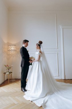 Damadın siyah takım elbiseli ilk buluşması ve beyaz gelinlikli gelinin beyaz ve siyah arka planda bir fotoğraf stüdyosunun içinde bir buket olması.