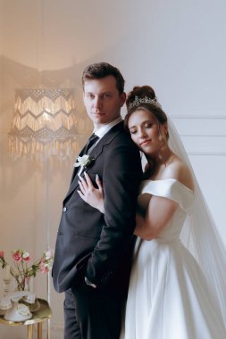 Damadın siyah takım elbiseli ilk buluşması ve beyaz gelinlikli gelinin beyaz ve siyah arka planda bir fotoğraf stüdyosunun içinde bir buket olması.