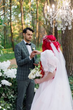 Güzel bir çift, yeşil takım elbiseli damat ve sıra dışı pembe gelinlikli gelin sonbaharda ormanda düzenlenen lüks bir açık hava seremonisinde poz veriyorlar.