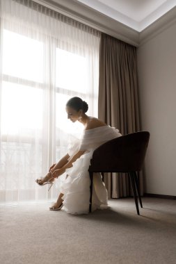 Günaydın ve lüks bir odada, pijama ve iç çamaşırlarıyla lüks ve güzel bir geline ayakkabı ve şık beyaz bir gelinlik giymeye hazırlanıyorum..