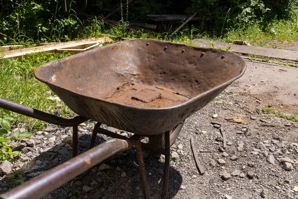 old, brown, rusted iron wheelbarrow with dents and holes