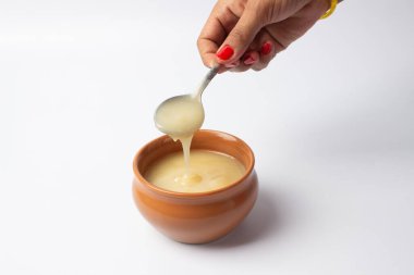 Beyaz arka planda seramik kasede elinde kahve kaşığıyla saf inek yağı.