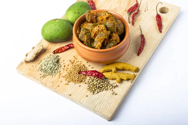 Indian mango pickle with green mango slices and spices with brown bowl on wooden board