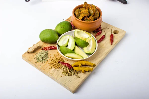 Indian mango pickle with green mango slices and spices with brown bowl on wooden board