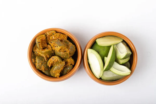 Indian mango pickle with green mango slices and spices on wooden board in brown bowl