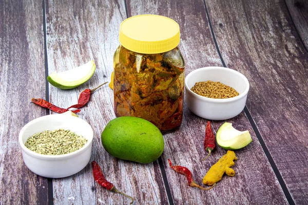 Indian mango pickle with green mango slices and spices with brown bowl on wooden background
