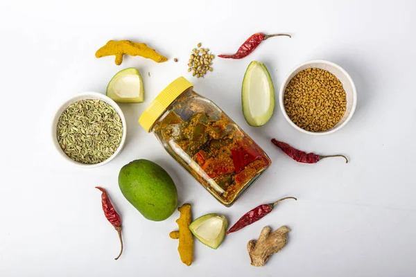 Indian mango pickle jar with green mango slices and spices with brown bowl on white background