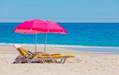 Plastik şezlonglar ve şemsiyeler Camps Bay, Cape Town 'daki kumlu sahilde.