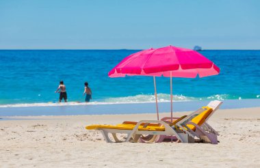 Plastik şezlonglar ve şemsiyeler Camps Bay, Cape Town 'daki kumlu sahilde.