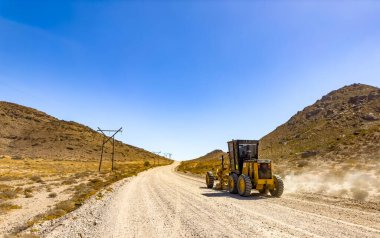 Richtersveld, South Africa - March 11, 2024: Large Caterpillar gravel dirt road grader smoothing out a road surface clipart